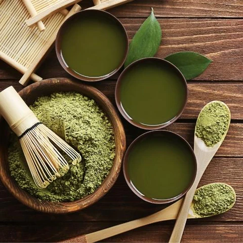 Matcha latte with matcha powder and bamboo whisk on a kitchen counter